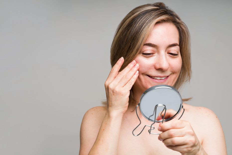 Woman happily examining her skin in a mirror, Linde Esthetics & Wellness Studio, Springfield MO