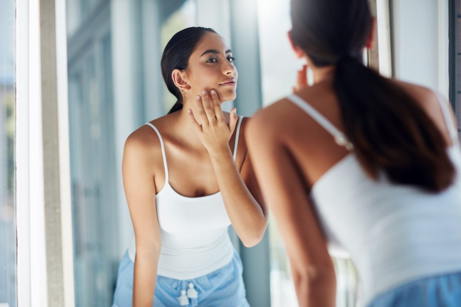 Young woman looking at skin in mirror, Linde Esthetics & Wellness Studio Springfield MO